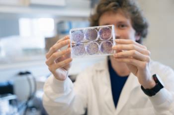 A scientist holds a tray with petri dishes, showing bacterial growth in a laboratory.