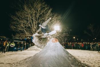 Snowboarder mid-air performing a trick at night, with a large crowd watching.