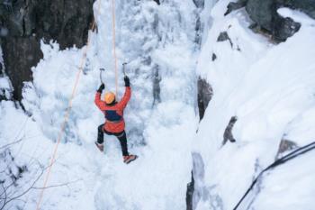 Climber in red gear scales a frozen waterfall in a snowy canyon.